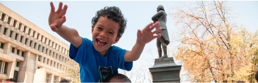 Image of a child with outstretched hands in front of Boston City Hall